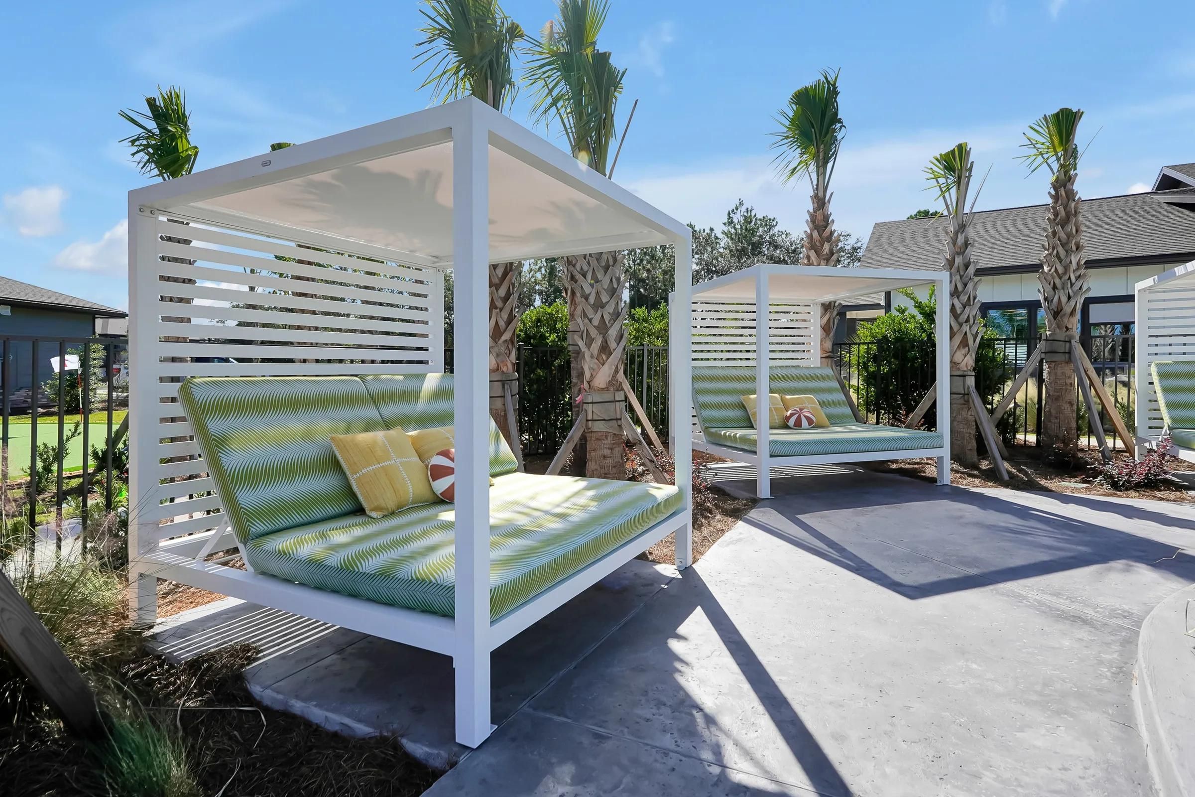 Two outdoor canopy lounge beds with green cushions and palm trees in the background on a sunny day.